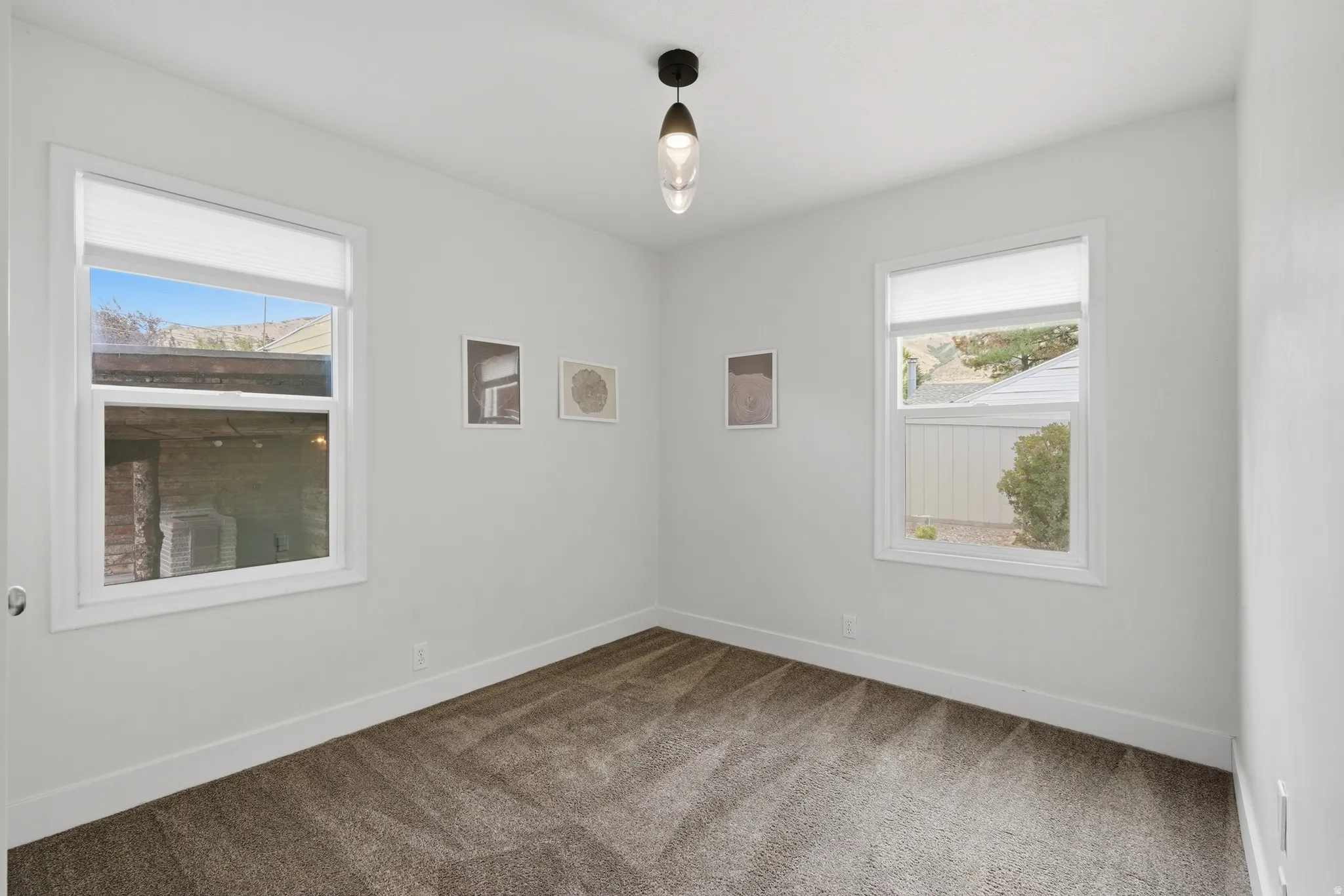 Bright room featuring two large windows with white blinds, neutral carpeting, and a contemporary ceiling light fixture