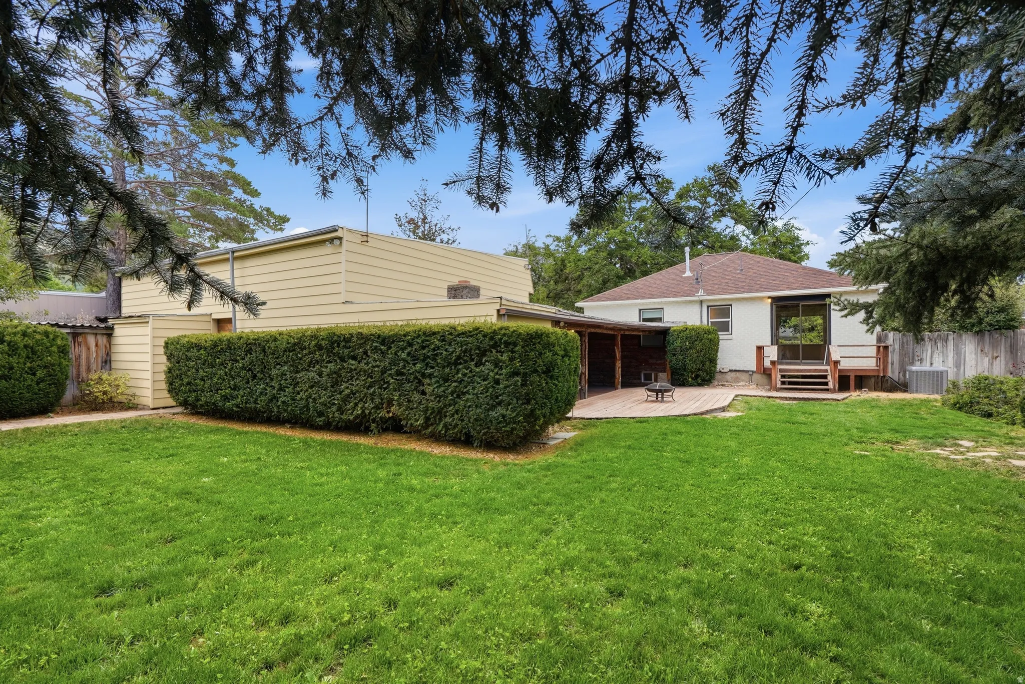 Expansive green lawn with a landscaped hedge, a wood deck patio, and a covered wood porch