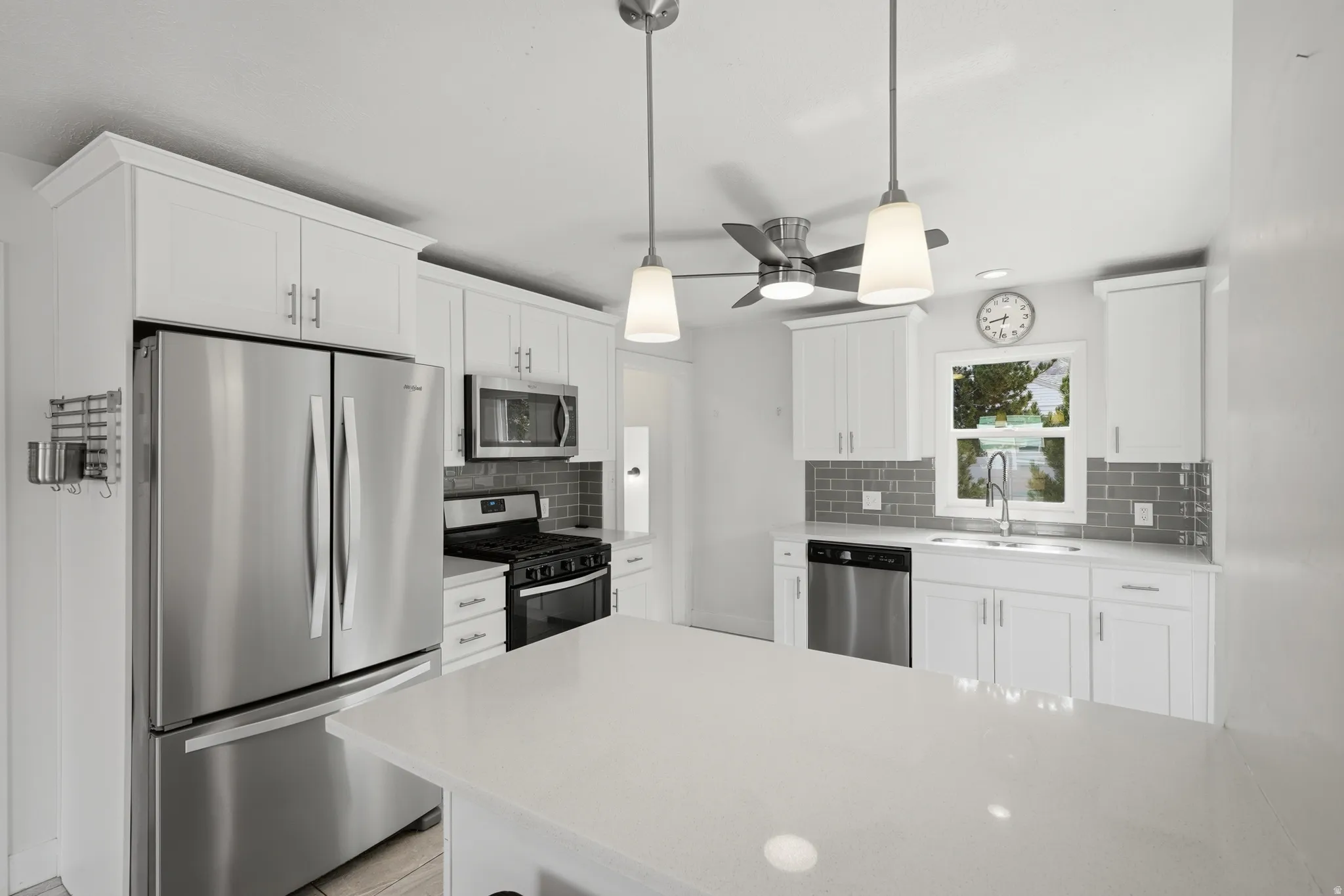 Kitchen featuring white cabinetry with silver hardware, stainless steel appliances, a subway tile backsplash, and a central island with a light-toned countertop