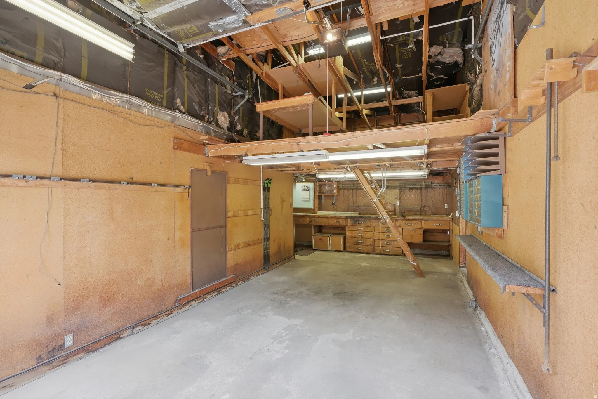 Spacious workshop area featuring exposed ceiling joists, concrete flooring, and built-in workbenches with integrated storage