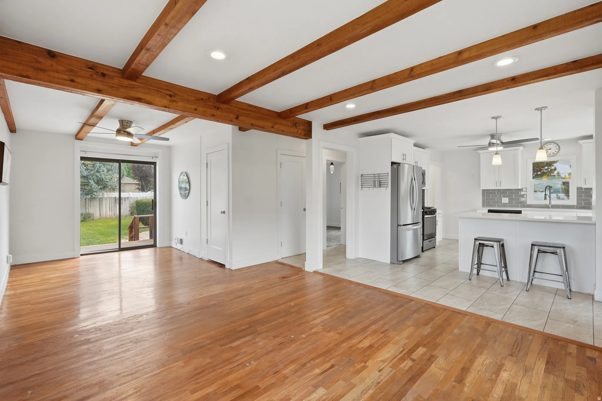 Open-concept living space featuring wood-finish flooring, exposed ceiling beams, and a sliding glass door to the backyard