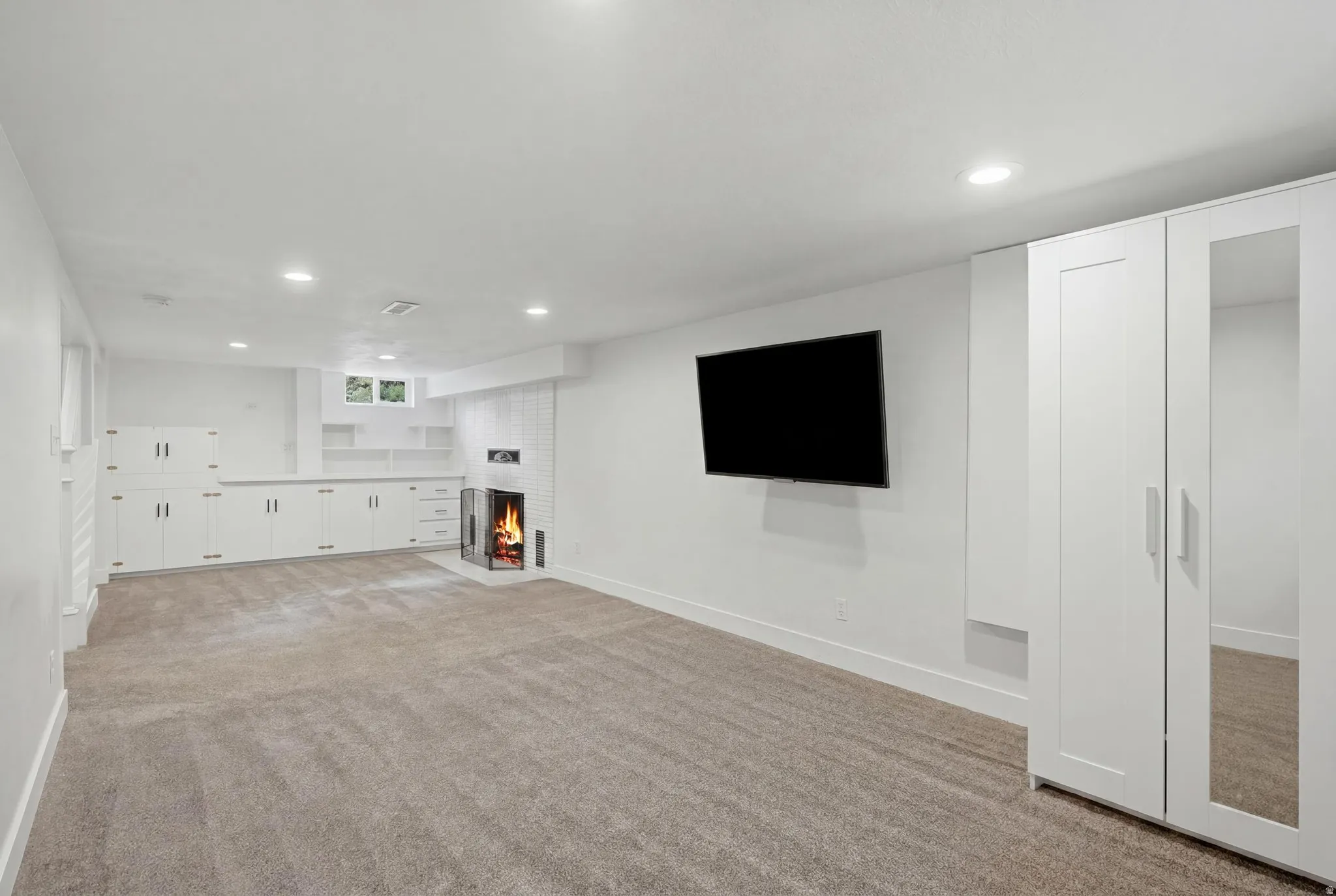 Spacious recreation room featuring recessed lighting, extensive built-in cabinetry, an electric fireplace, and plush carpet flooring