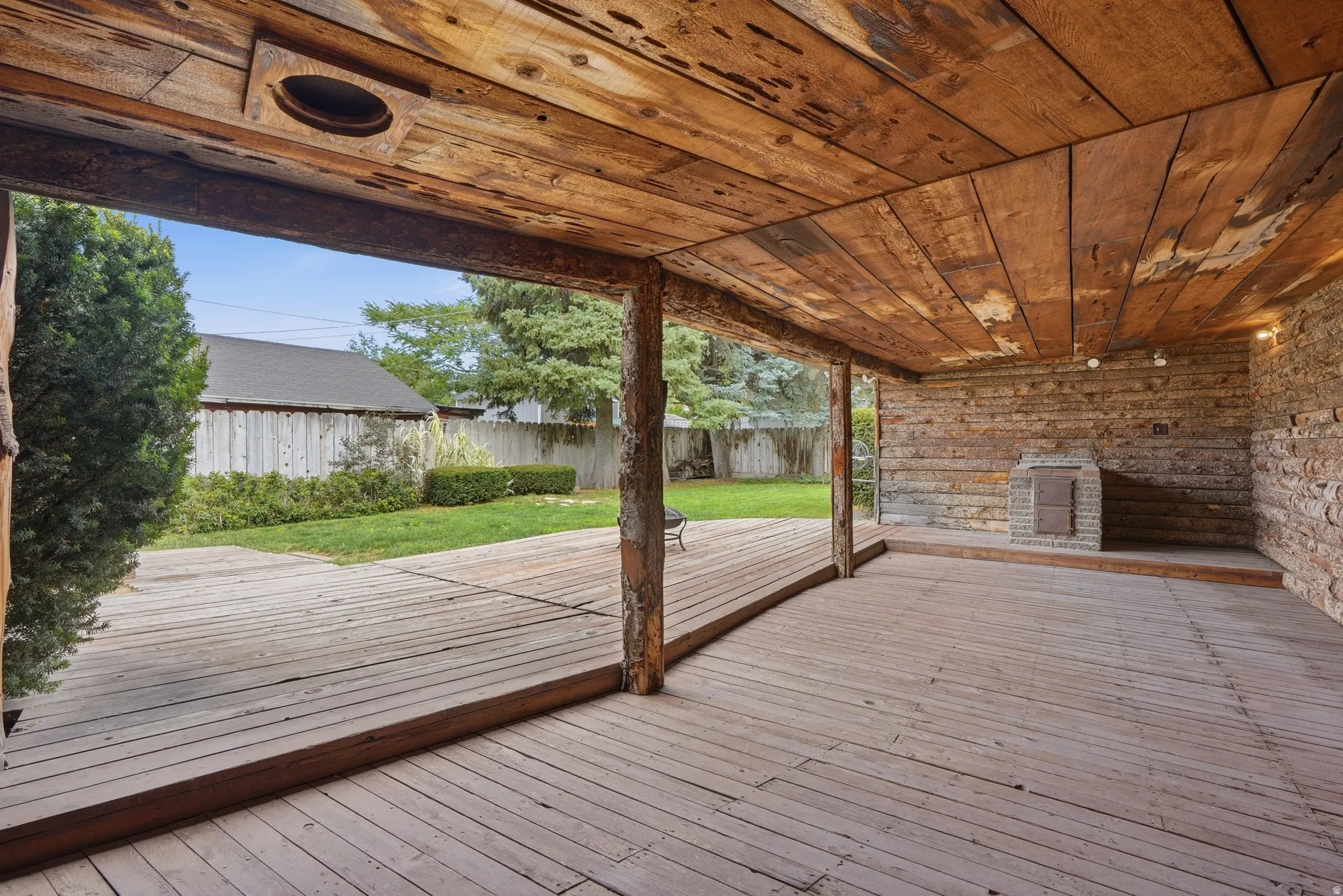 Expansive covered patio featuring wood plank flooring and ceiling, a built-in stone fireplace, and exposed wood support beams