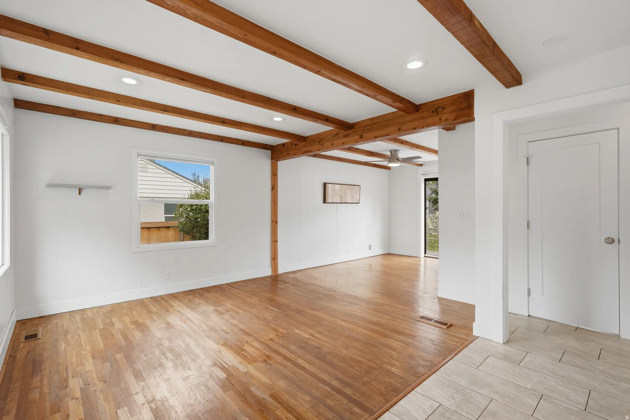 Spacious room featuring exposed wood beams, wood-finish flooring, recessed lighting, and a window with natural light