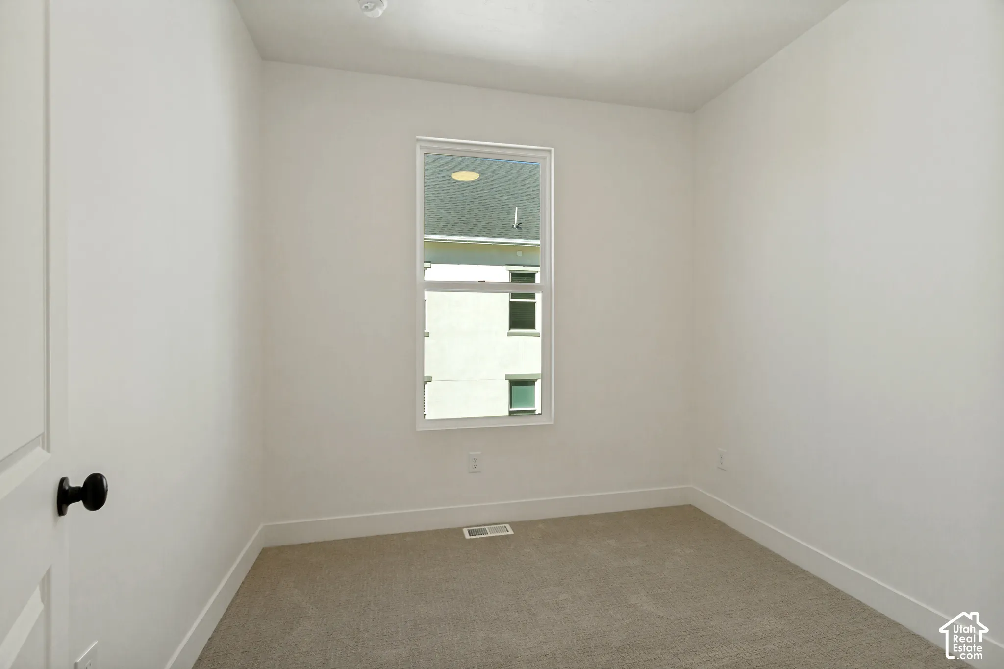 Neutral-toned carpeting, white walls, and a single window with white trim