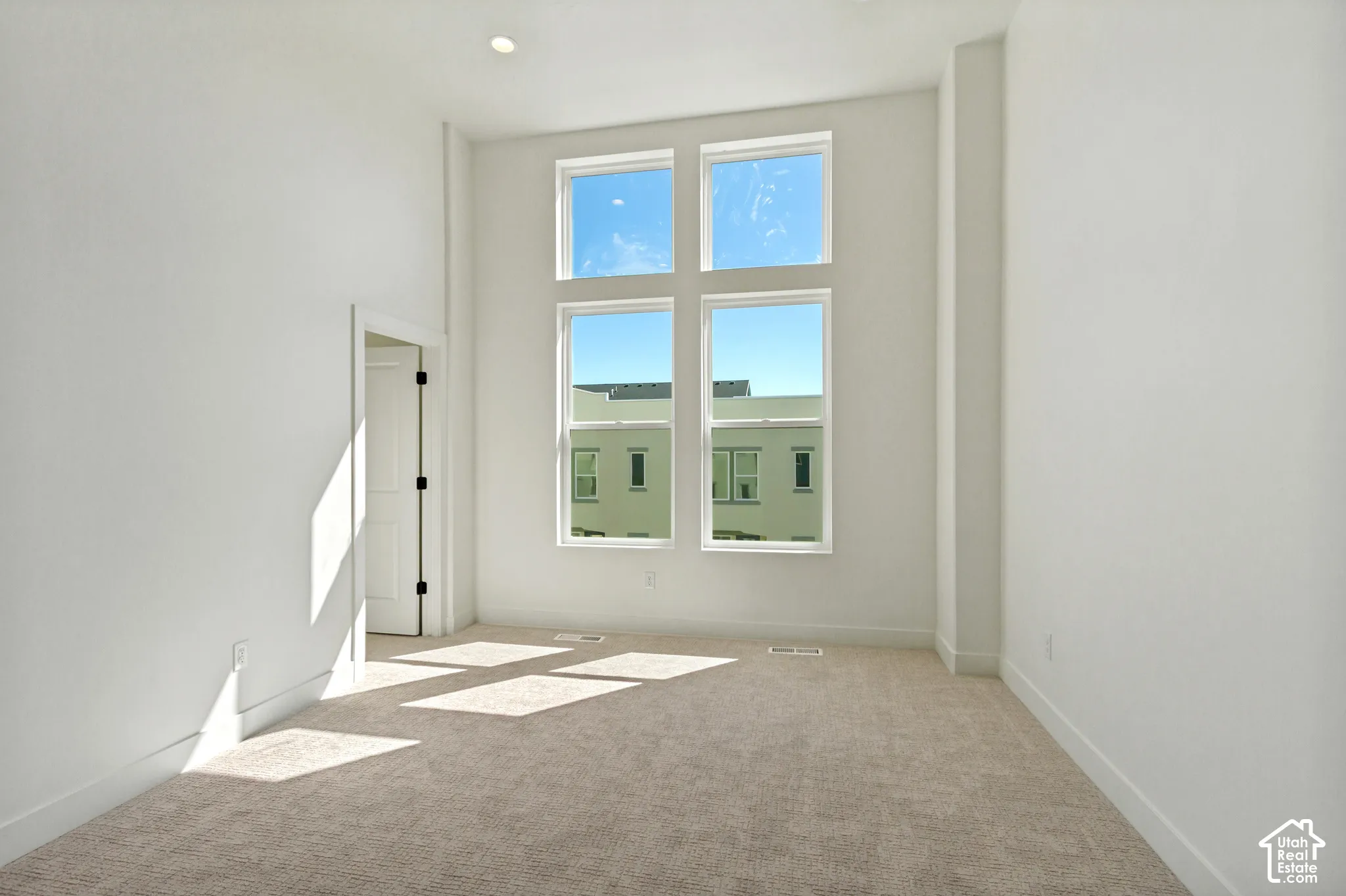 Tall ceilings, recessed ceiling light, multi-pane window configuration, light-colored carpeting, and a white interior door