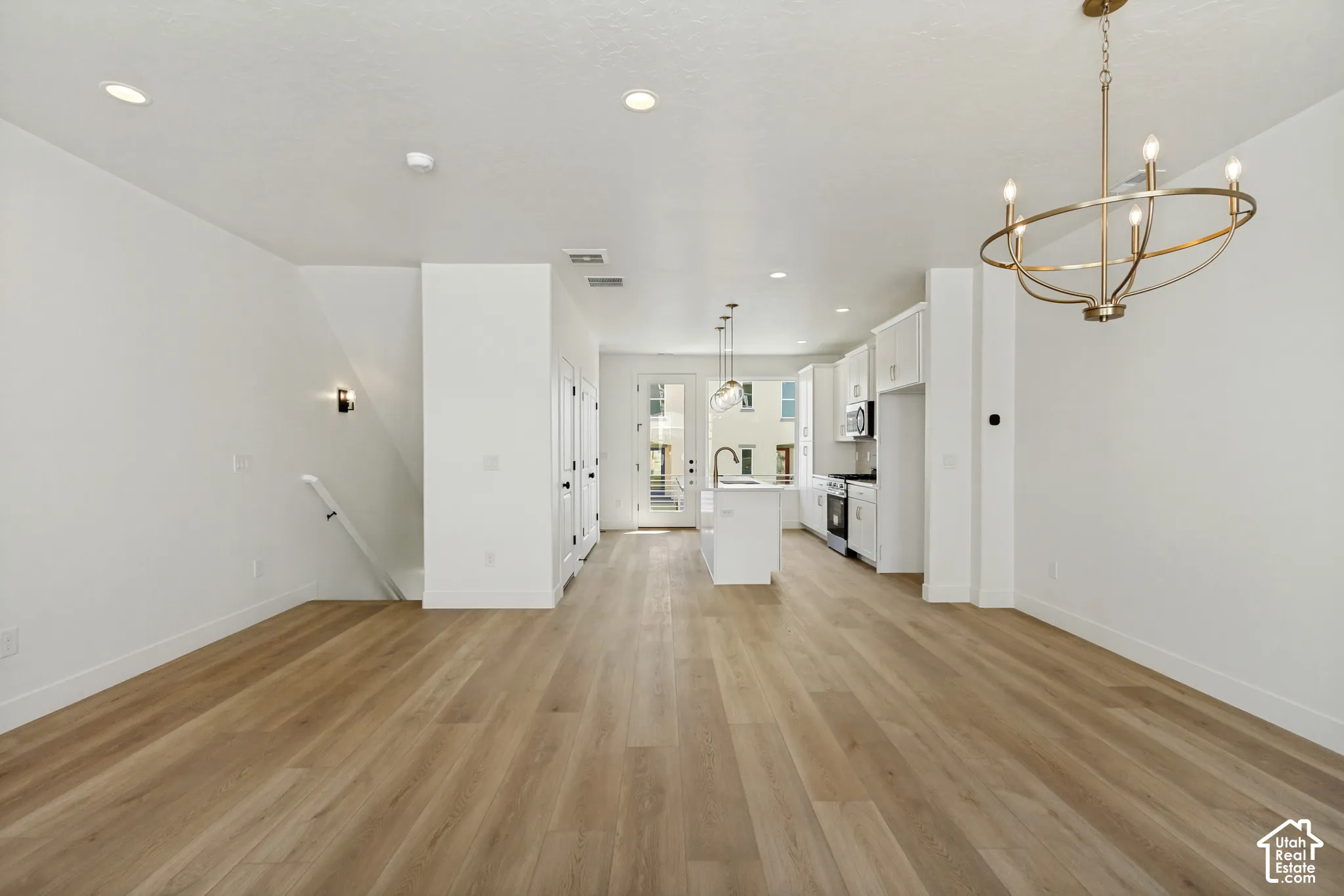 Open-concept living space featuring wood-finish flooring, recessed lighting, a modern brass chandelier, white cabinetry, and stainless steel appliances