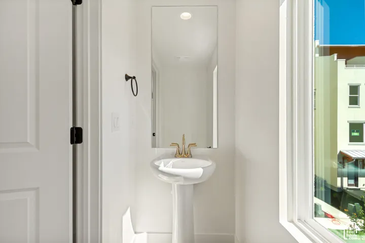 Pedestal sink with brass-finish faucet, rectangular wall mirror, and large window