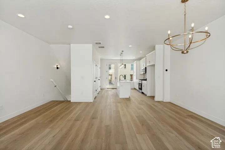 Open-concept living space featuring wood-finish flooring, recessed lighting, a modern brass chandelier, white cabinetry, and stainless steel appliances