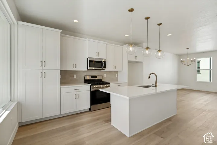 White shaker cabinetry, stainless steel appliances, central kitchen island with sink, wood-finish flooring, and recessed lighting