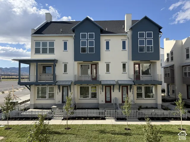 Contemporary townhome exterior featuring a blue siding accent, a covered balcony, and a white picket fence