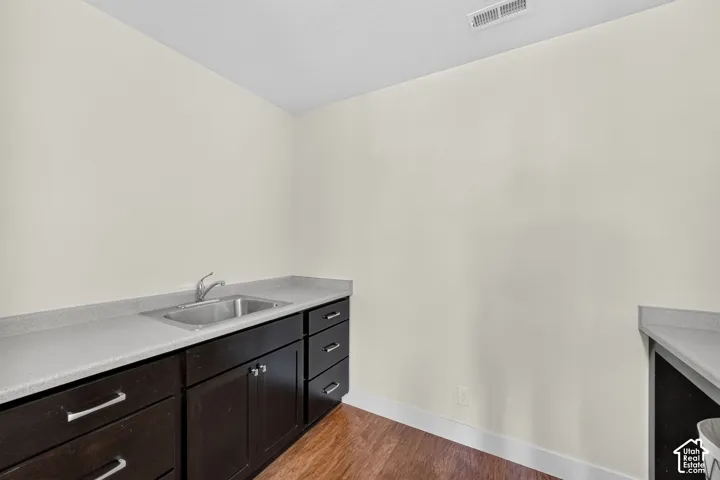Service area featuring a stainless steel sink, dark wood-finish cabinetry, light grey countertops, and wood-finish flooring
