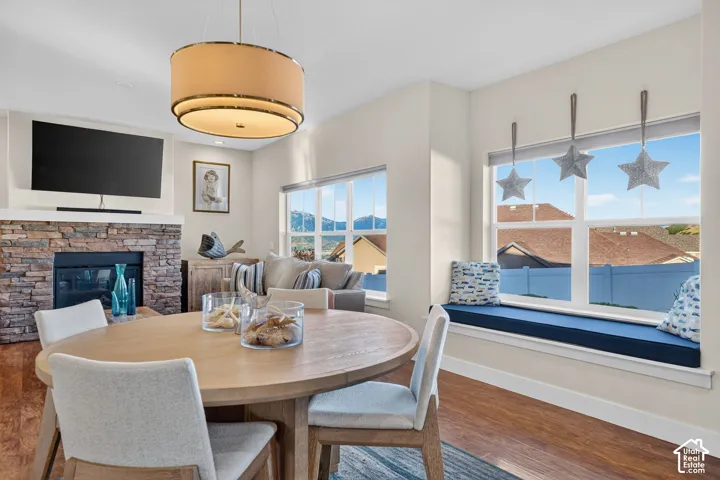 Open-concept dining and living area featuring a stone-clad fireplace, wood-finish flooring, and a built-in window seat