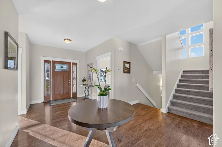 Spacious entryway featuring rich wood-finish flooring, a wood entry door with decorative glass sidelights, and a staircase with neutral carpeting