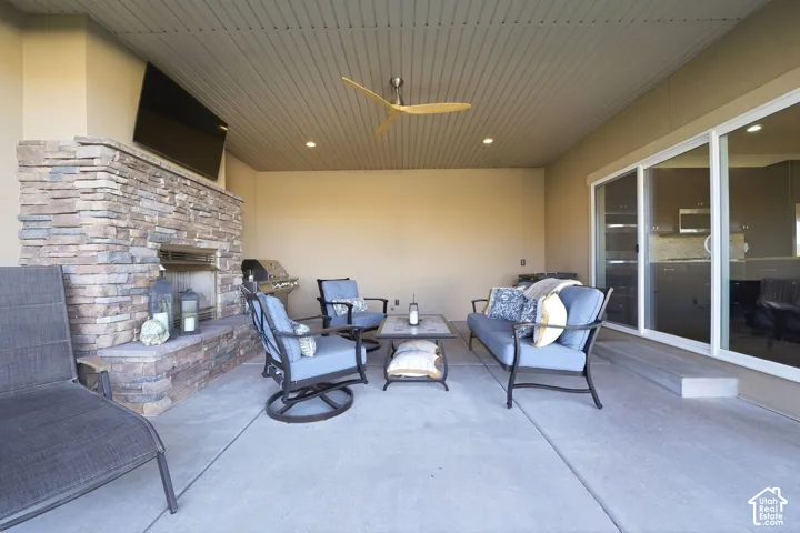 Covered outdoor patio featuring a stone-clad fireplace with an integrated media niche, a slatted ceiling with recessed lighting, and a modern ceiling fan