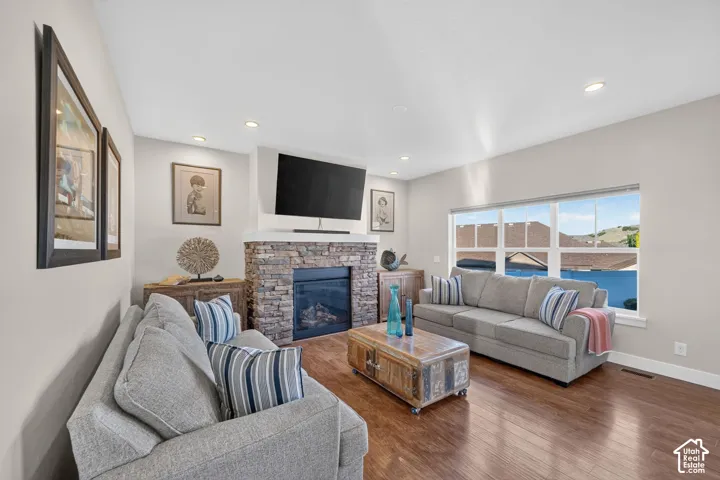 Spacious living area featuring a stone-clad fireplace with a hearth, wood-finish flooring, a large multi-pane window, recessed lighting, and light-toned walls