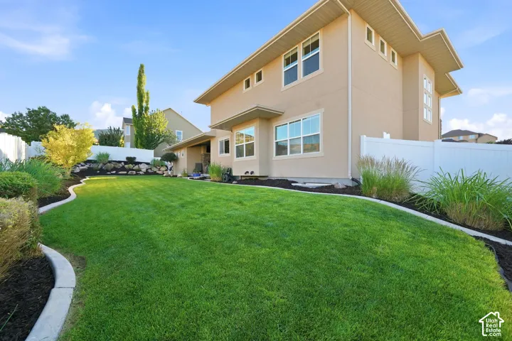 Expansive backyard featuring a manicured lawn, established landscaping, and a tan stucco exterior