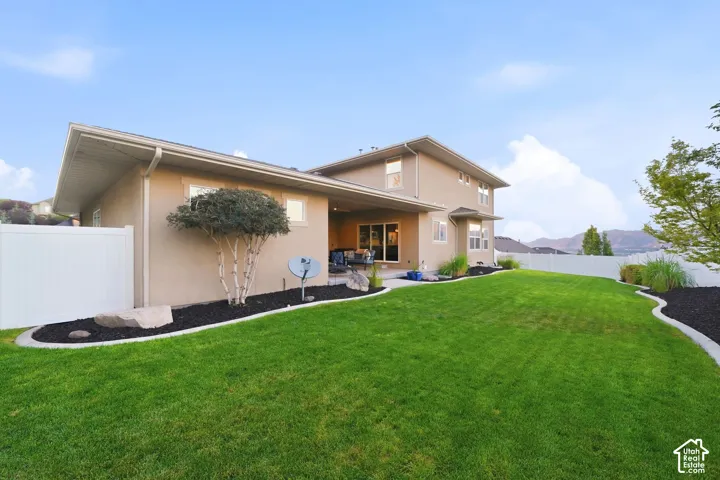 Expansive backyard featuring a manicured lawn, white vinyl fencing, and mature landscaping