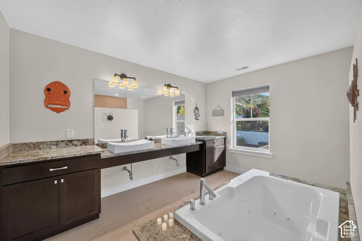 Bathroom featuring a built-in jetted tub, dual vanity with vessel sinks, dark wood cabinetry, and granite countertops