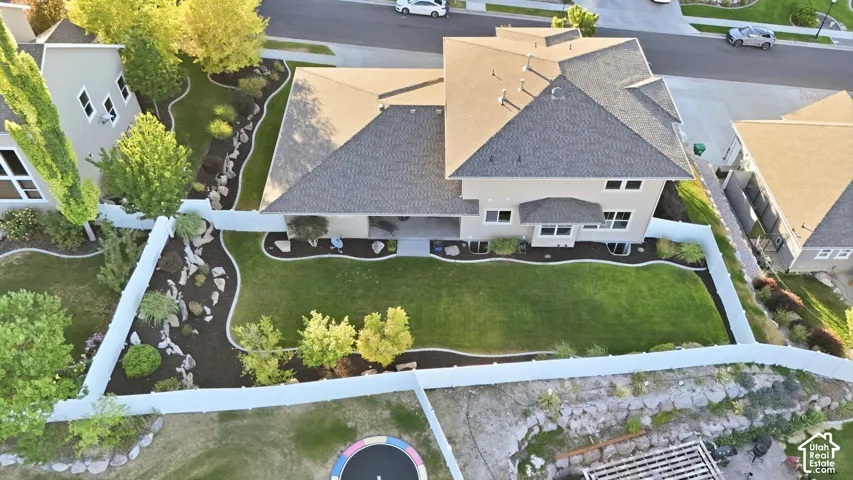 Expansive backyard featuring a manicured lawn, established landscaping beds, and a white privacy fence