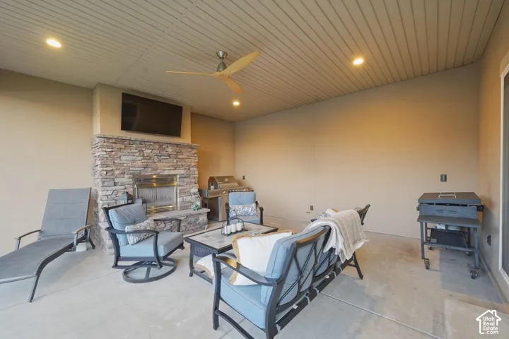 Covered patio featuring a stone-clad fireplace, integrated television, and a wood-bladed ceiling fan