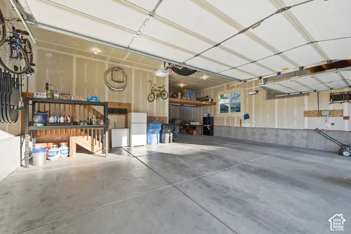 Spacious garage with multiple garage doors, concrete flooring, built-in shelving, a finished ceiling, and an upper storage shelf