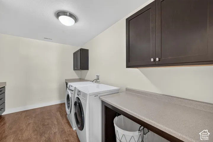 Laundry area featuring wood-finish flooring, light-colored walls, dark wood cabinetry, and a light-toned countertop