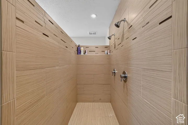 Walk-in shower featuring wood-finish tile, dual showerheads, polished chrome fixtures, and an integrated shelf
