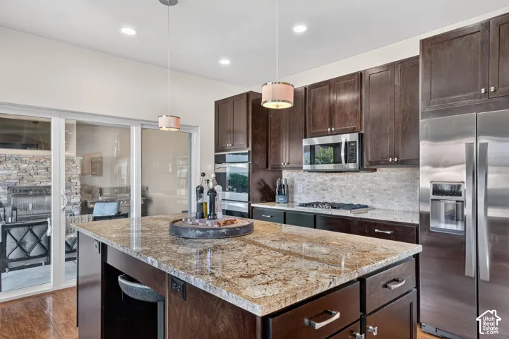 Kitchen featuring a large island with a stone countertop, dark wood cabinetry, stainless steel appliances, and a tile backsplash