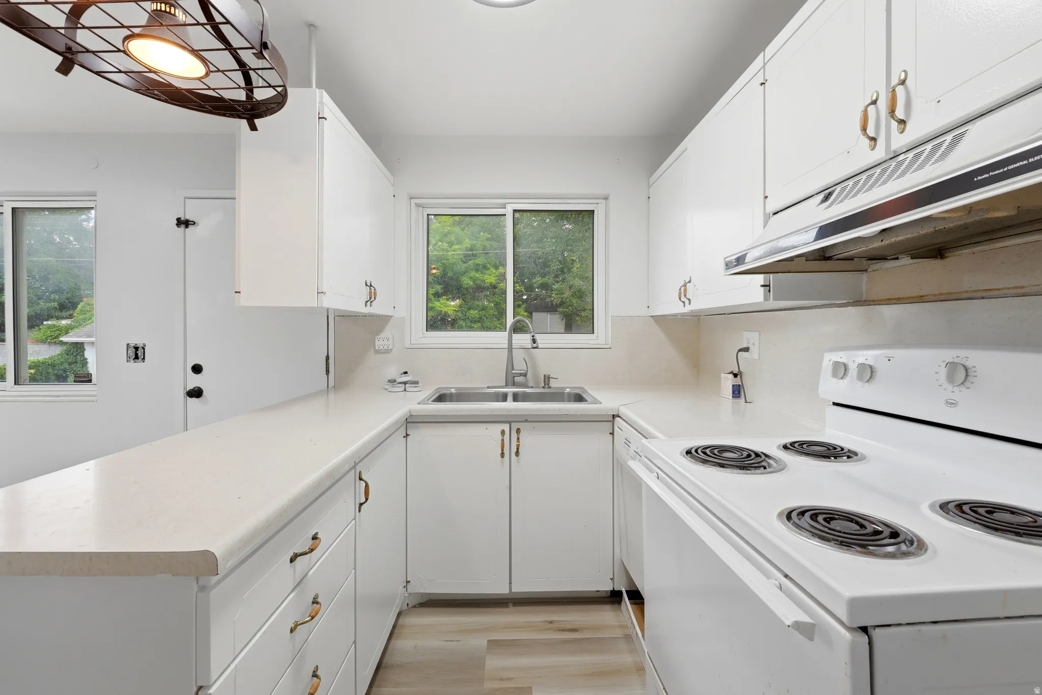 Bright kitchen featuring white cabinetry and countertops, a double basin stainless steel sink, a four-burner electric range with an overhead vent, and wood-finish flooring
