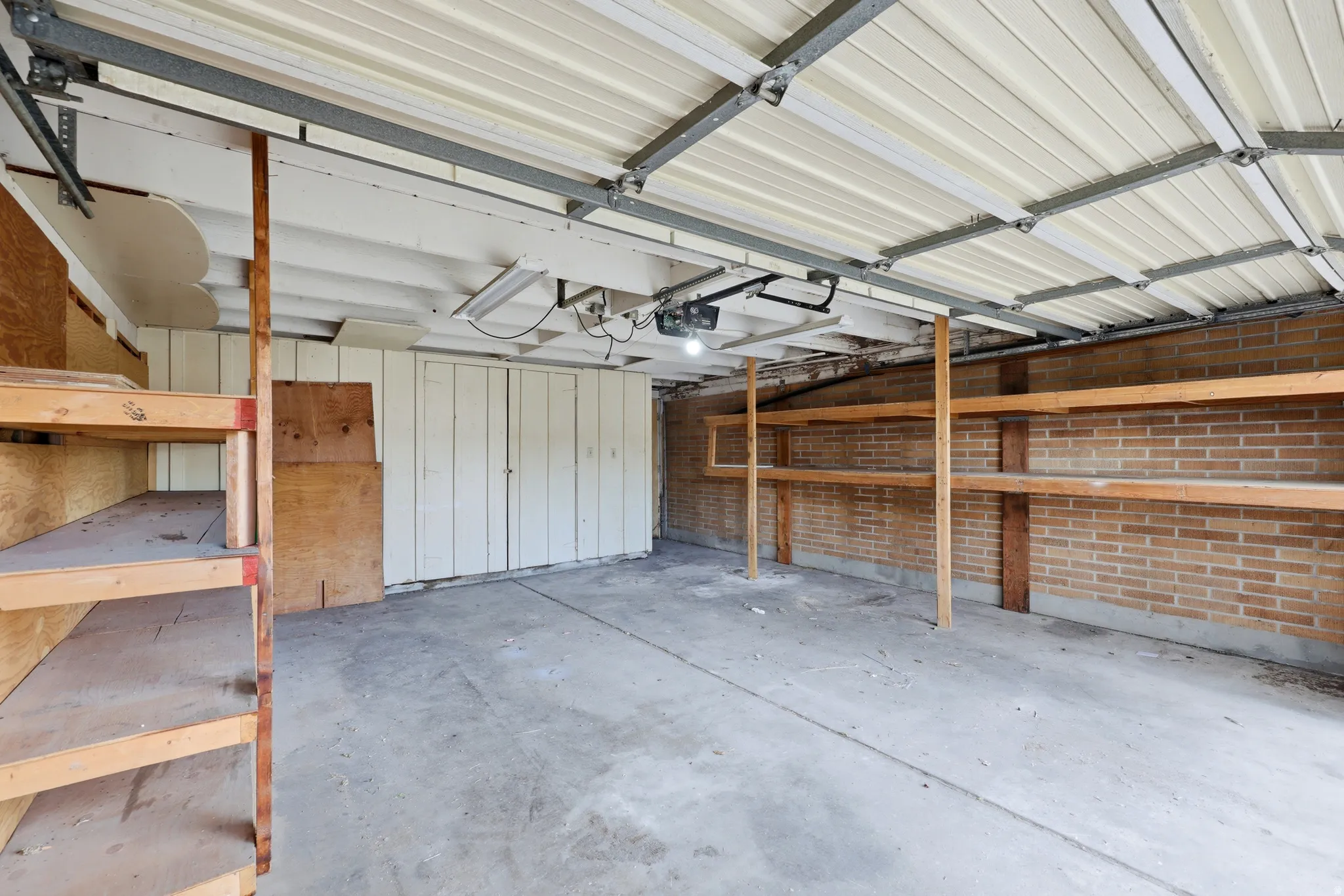 Spacious garage featuring a concrete floor, brick wall, built-in shelving, white paneling, and an overhead garage door mechanism
