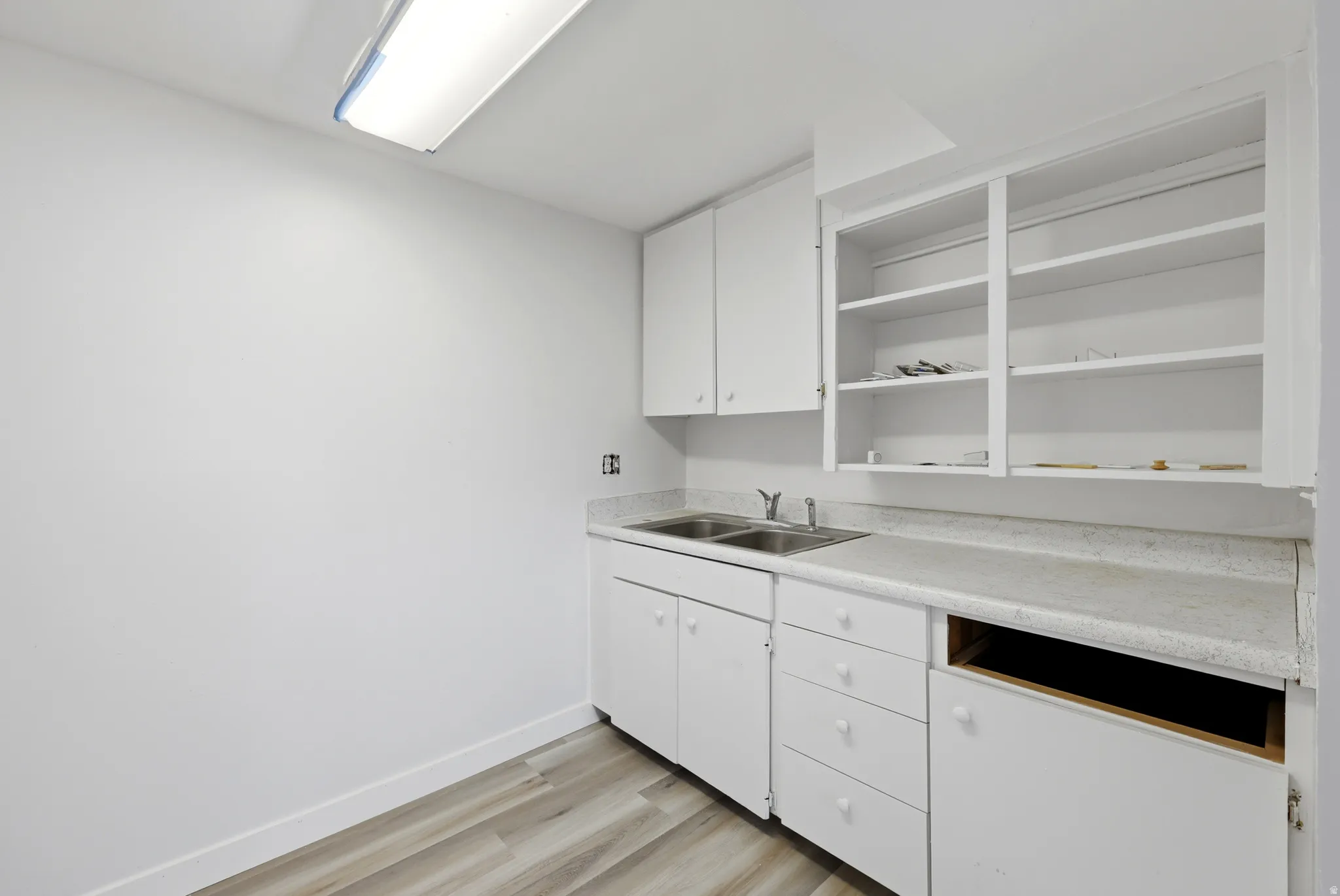 Kitchenette featuring white cabinetry, a double basin stainless steel sink, light-toned countertops, and wood-finish flooring