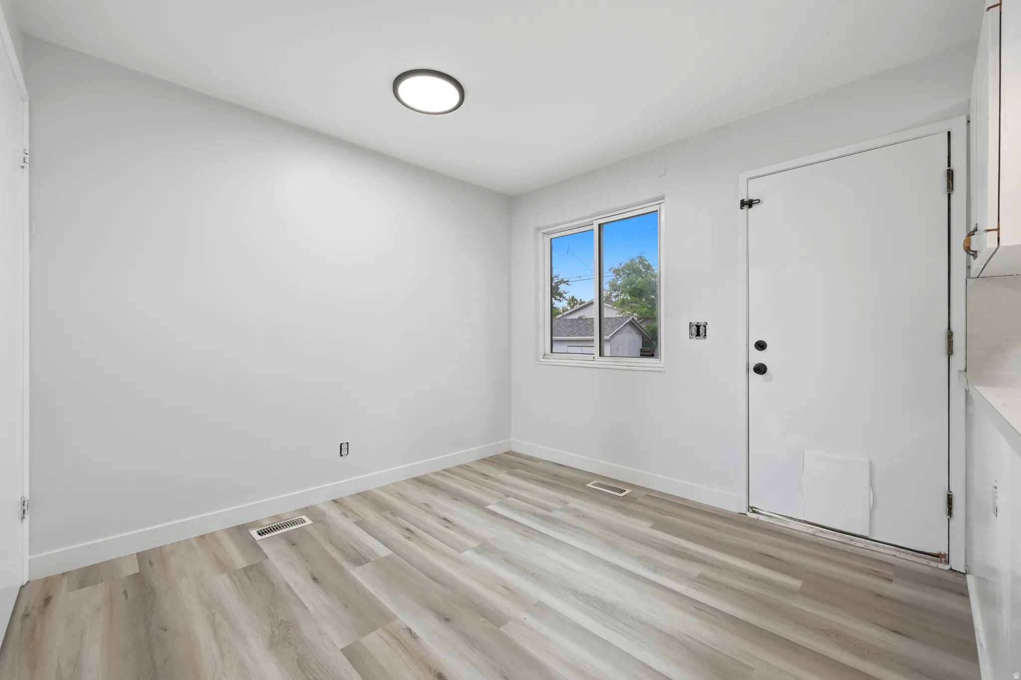 Spacious room featuring light wood-finish flooring, white walls, and a recessed ceiling light fixture