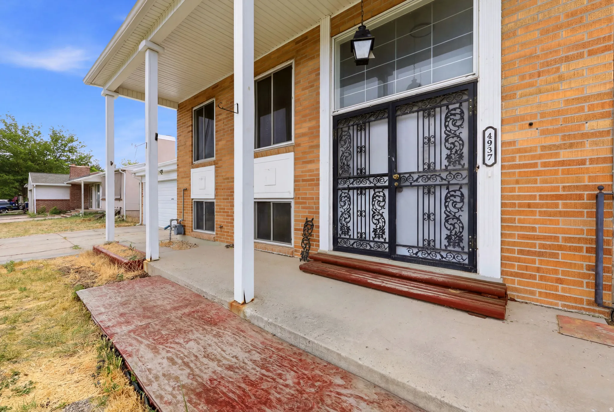 Brick facade residence featuring a covered front porch with white columns, an ornate black metal security door, and a transom window above the entry