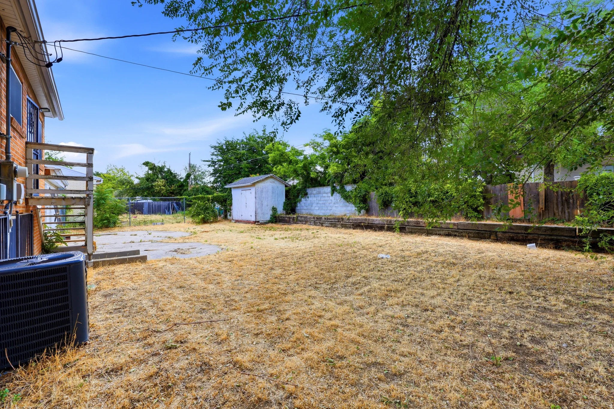 Spacious backyard featuring a storage shed, concrete patio area, and mature perimeter trees