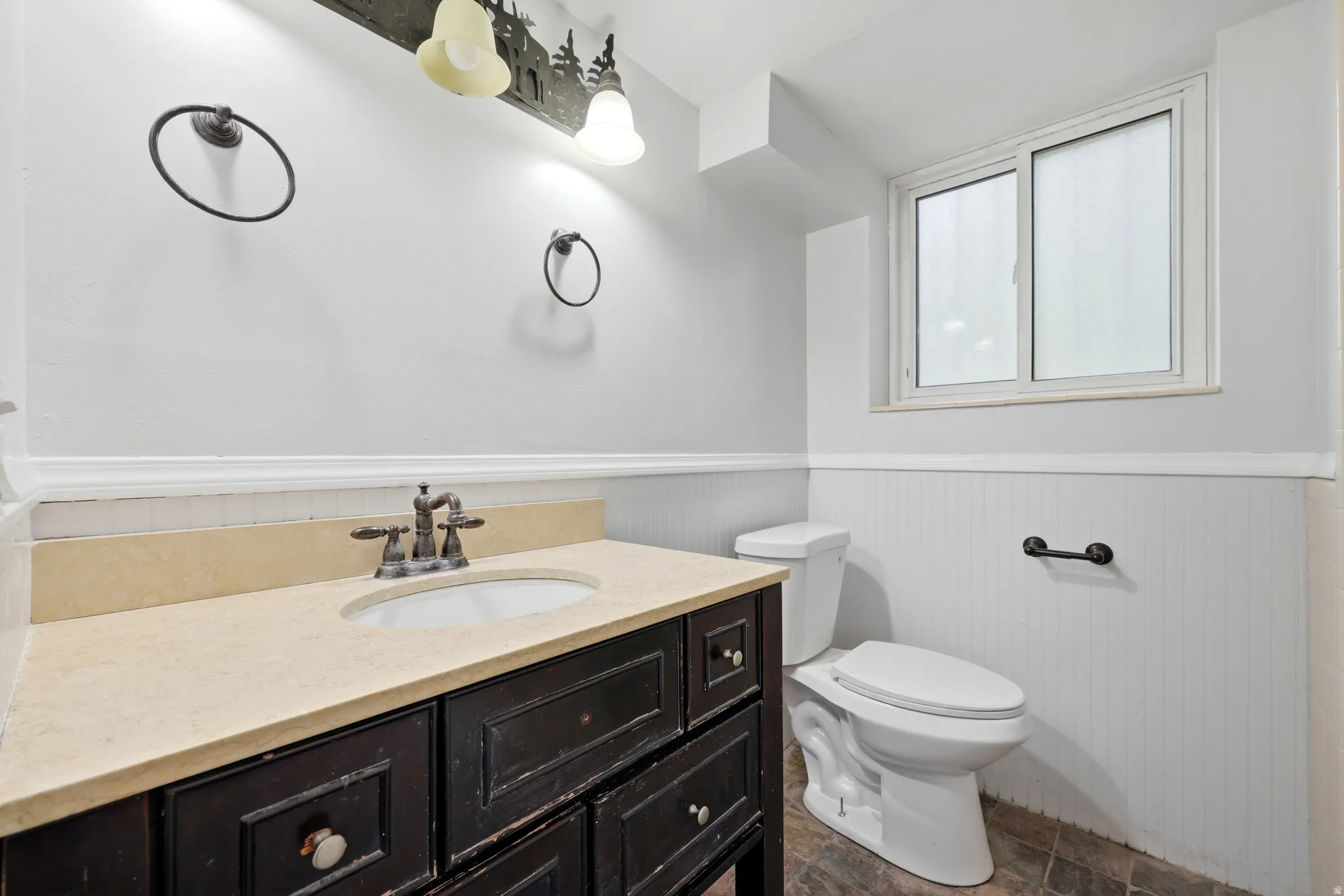 Bathroom featuring a dark wood-finish vanity with an undermount sink and light-toned countertop, a contemporary toilet, and a window providing natural illumination