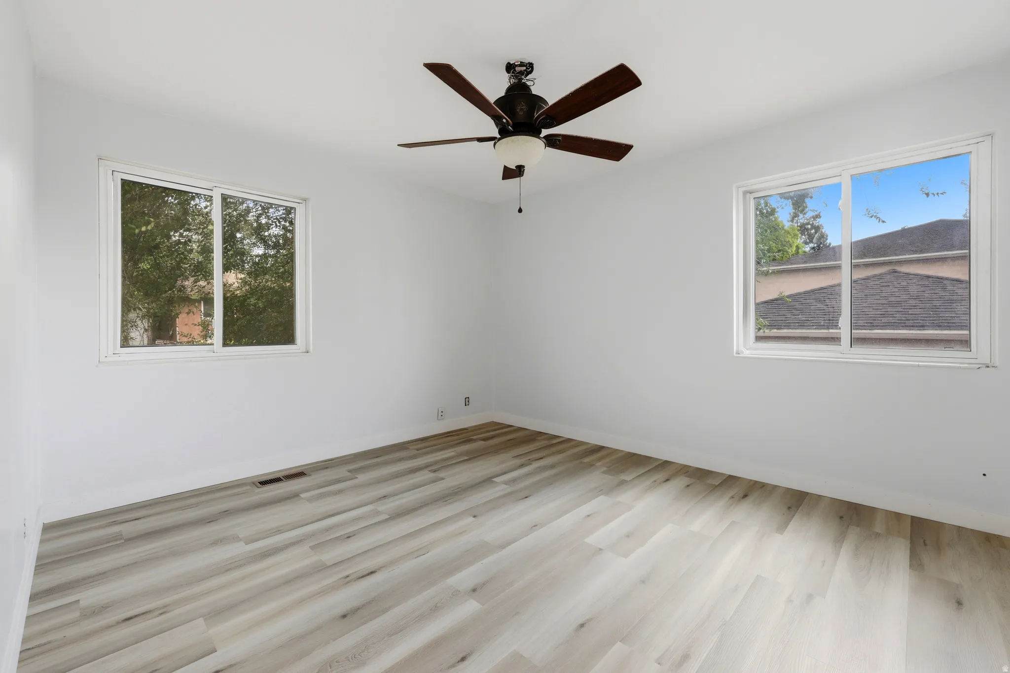 Light-filled interior featuring two windows, wood-finish flooring, a ceiling fan with integrated lighting, and neutral wall tones