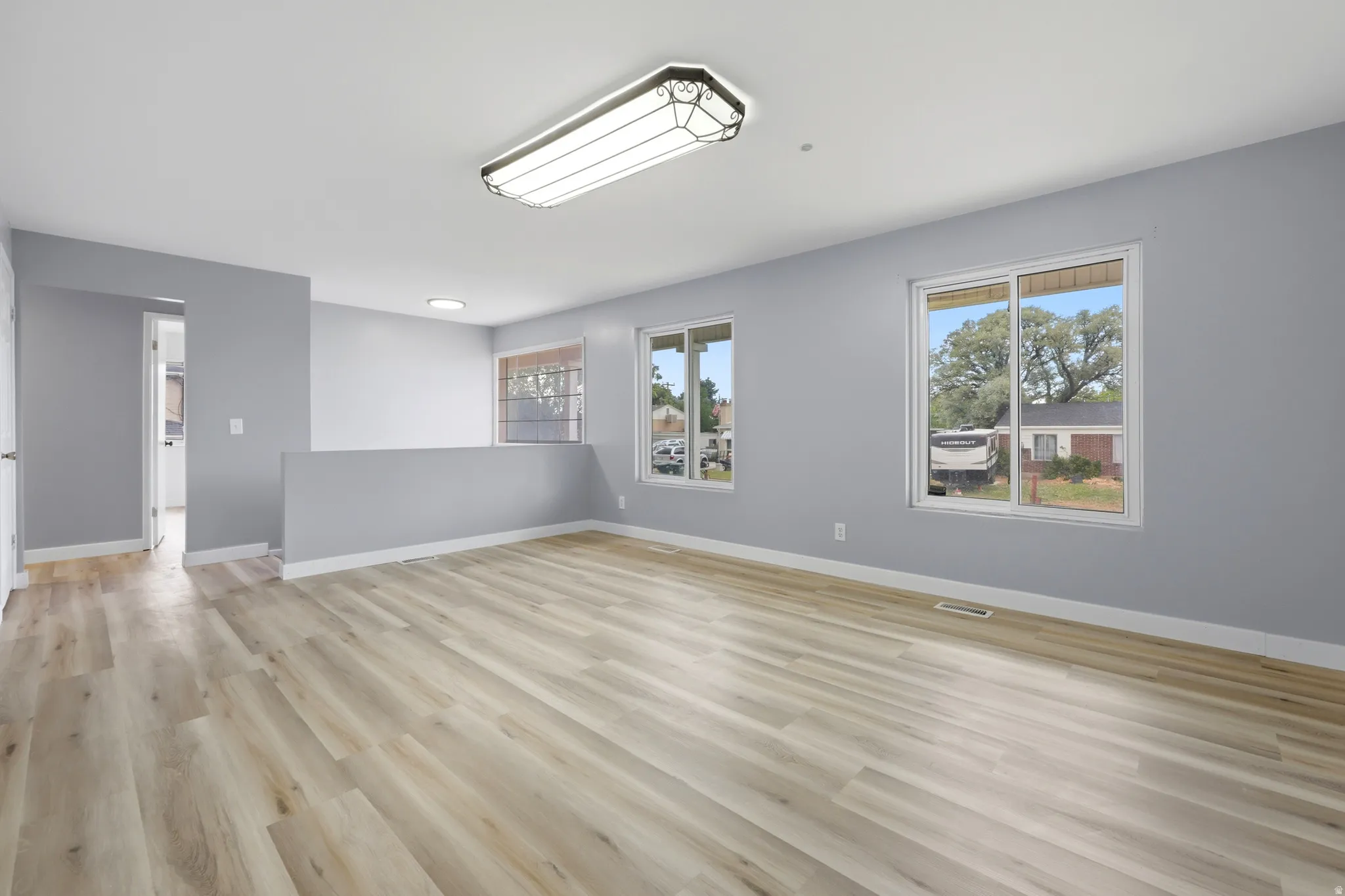 Spacious room featuring light wood-finish flooring, two large windows, white baseboards, and a contemporary ceiling light fixture