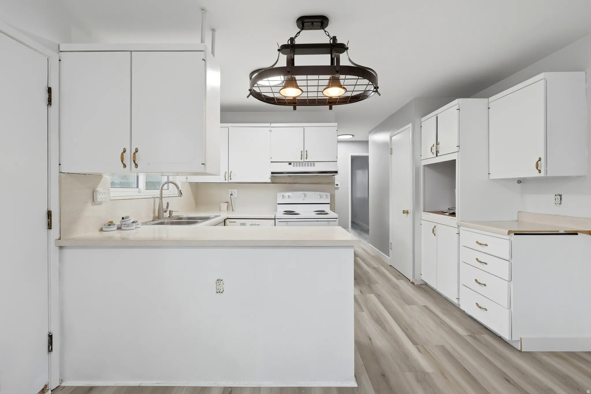 Bright kitchen featuring white cabinetry, light-toned countertops, and wood-finish flooring