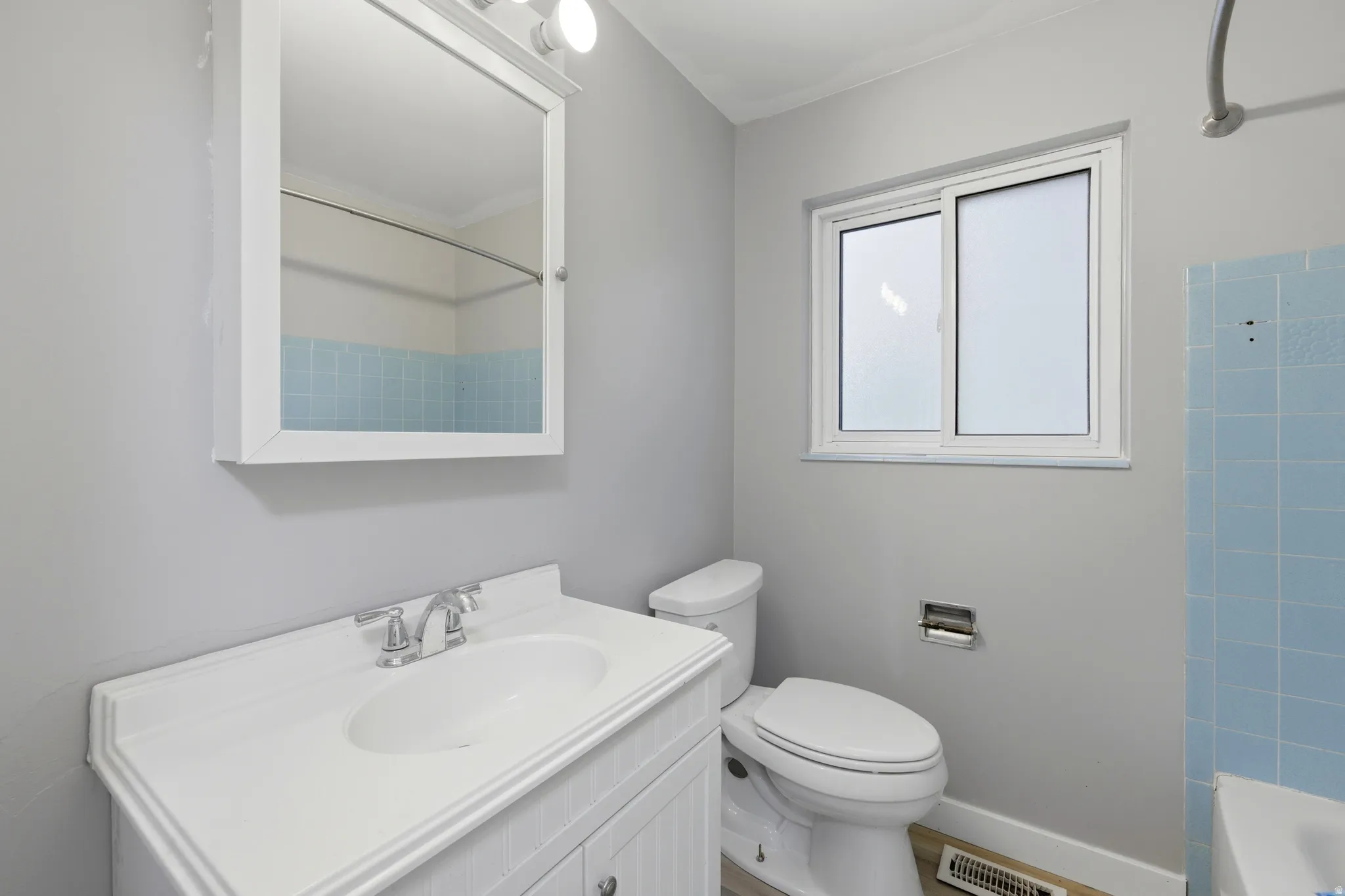 Bathroom featuring a white vanity with integrated sink, chrome faucet, wall-mounted medicine cabinet with integrated lighting, and a sliding window