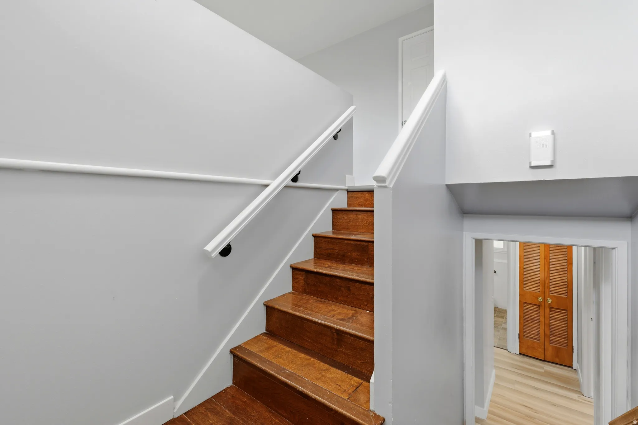 Staircase featuring wood-finish treads and risers, white handrails with black mounts, and light gray wall finishes