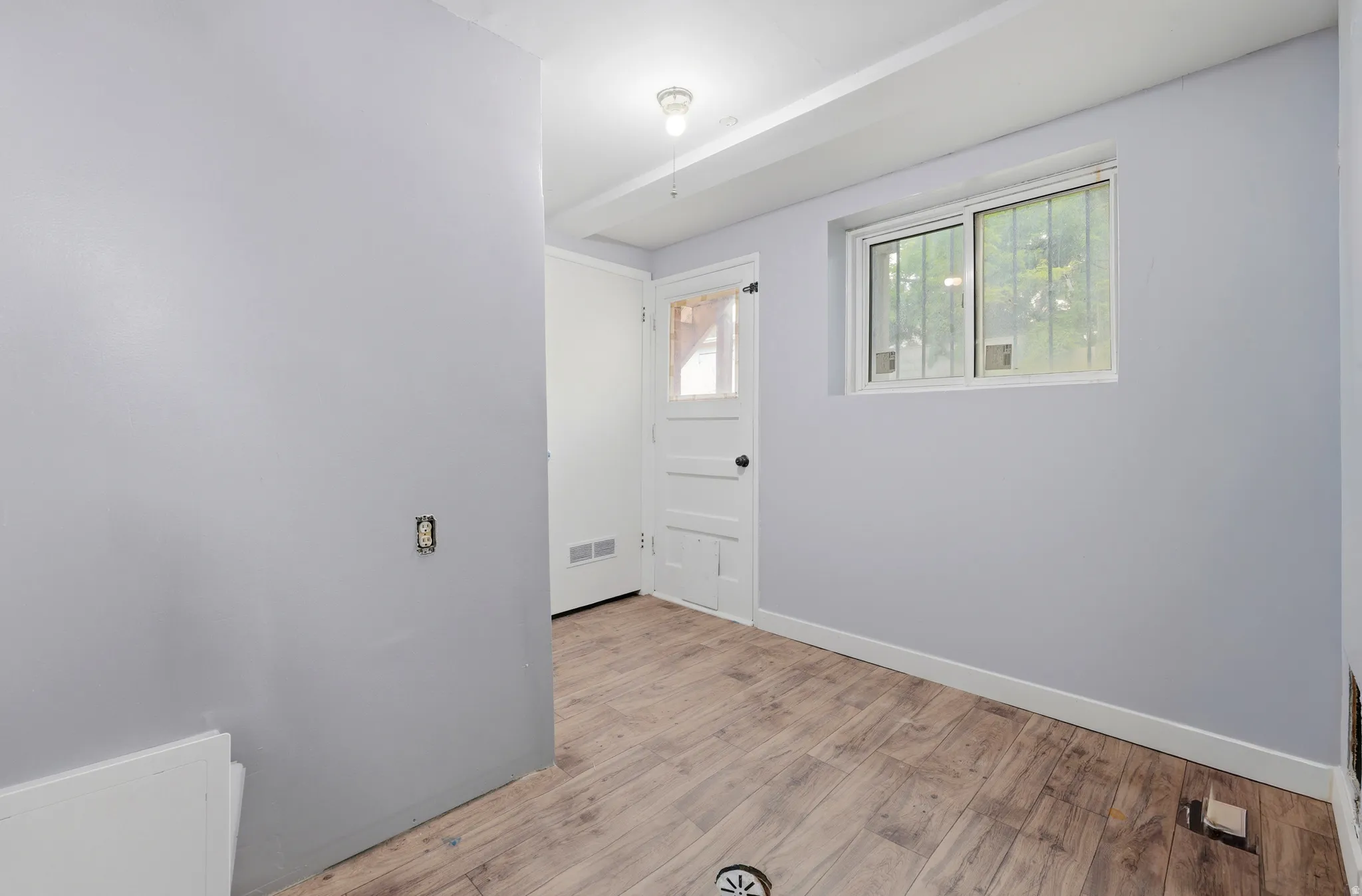 Room featuring wood-finish flooring, a white paneled door, and a single window with white trim