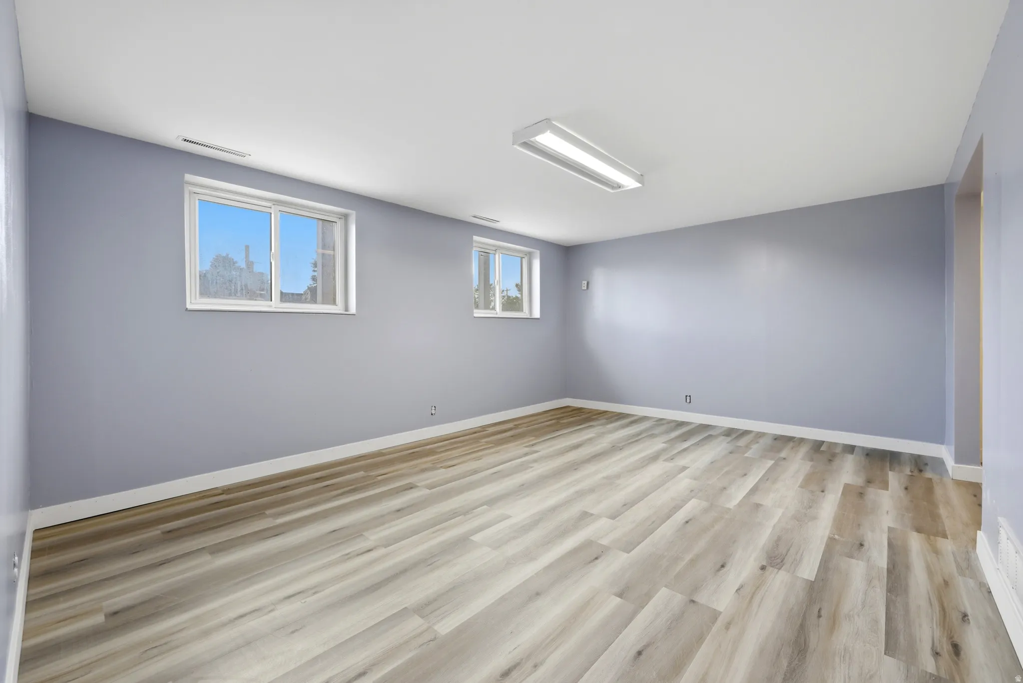 Spacious room featuring wood-finish flooring, light blue walls, and white trim