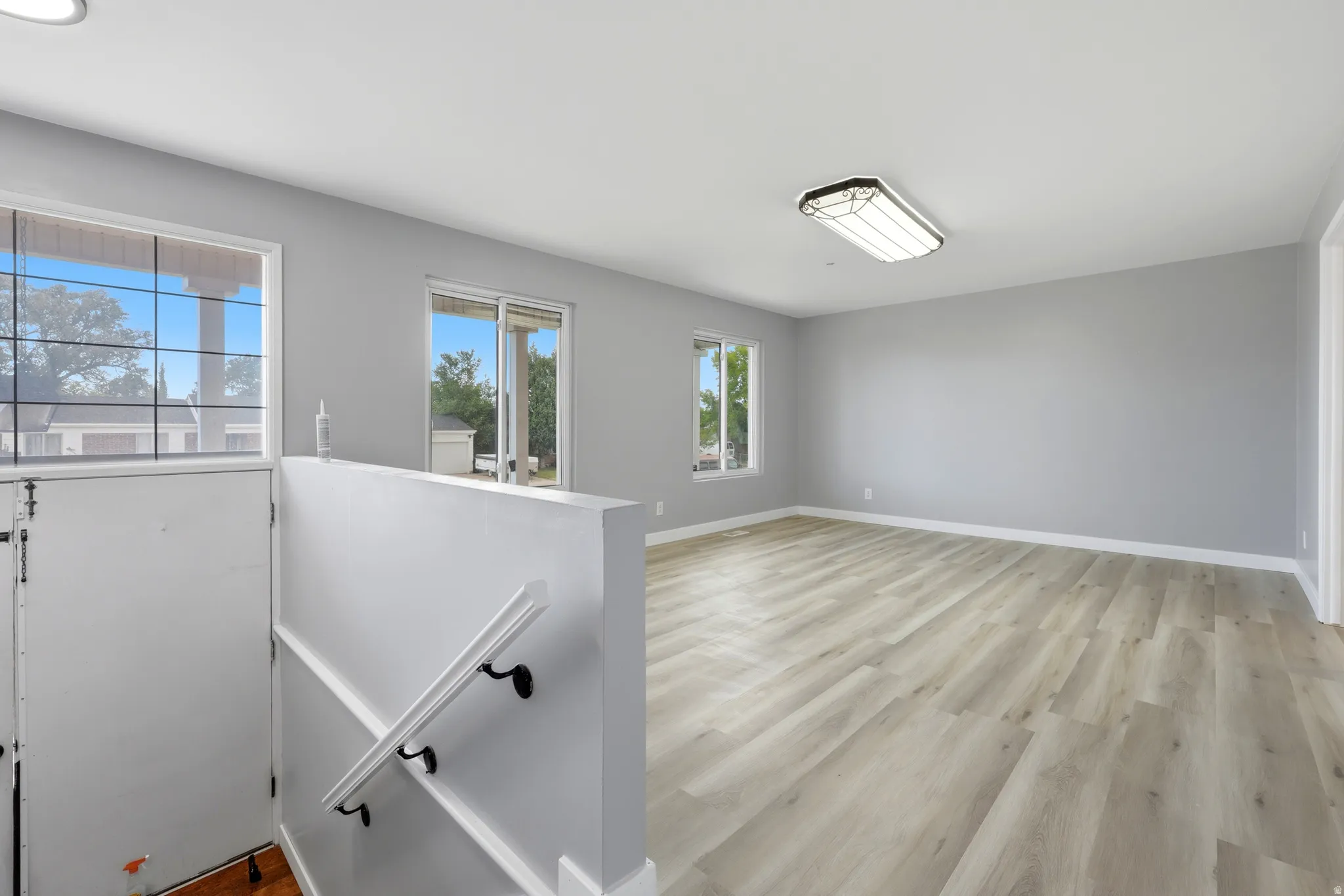 Spacious room featuring light wood-finish flooring, neutral gray wall paint, multiple windows, and a sliding glass door