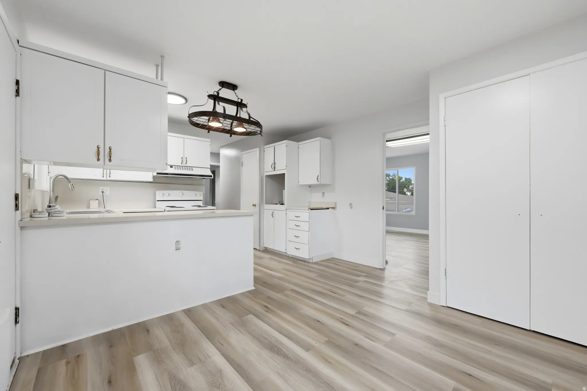 Kitchen area featuring wood-finish flooring, white cabinetry, and a black metal-frame chandelier