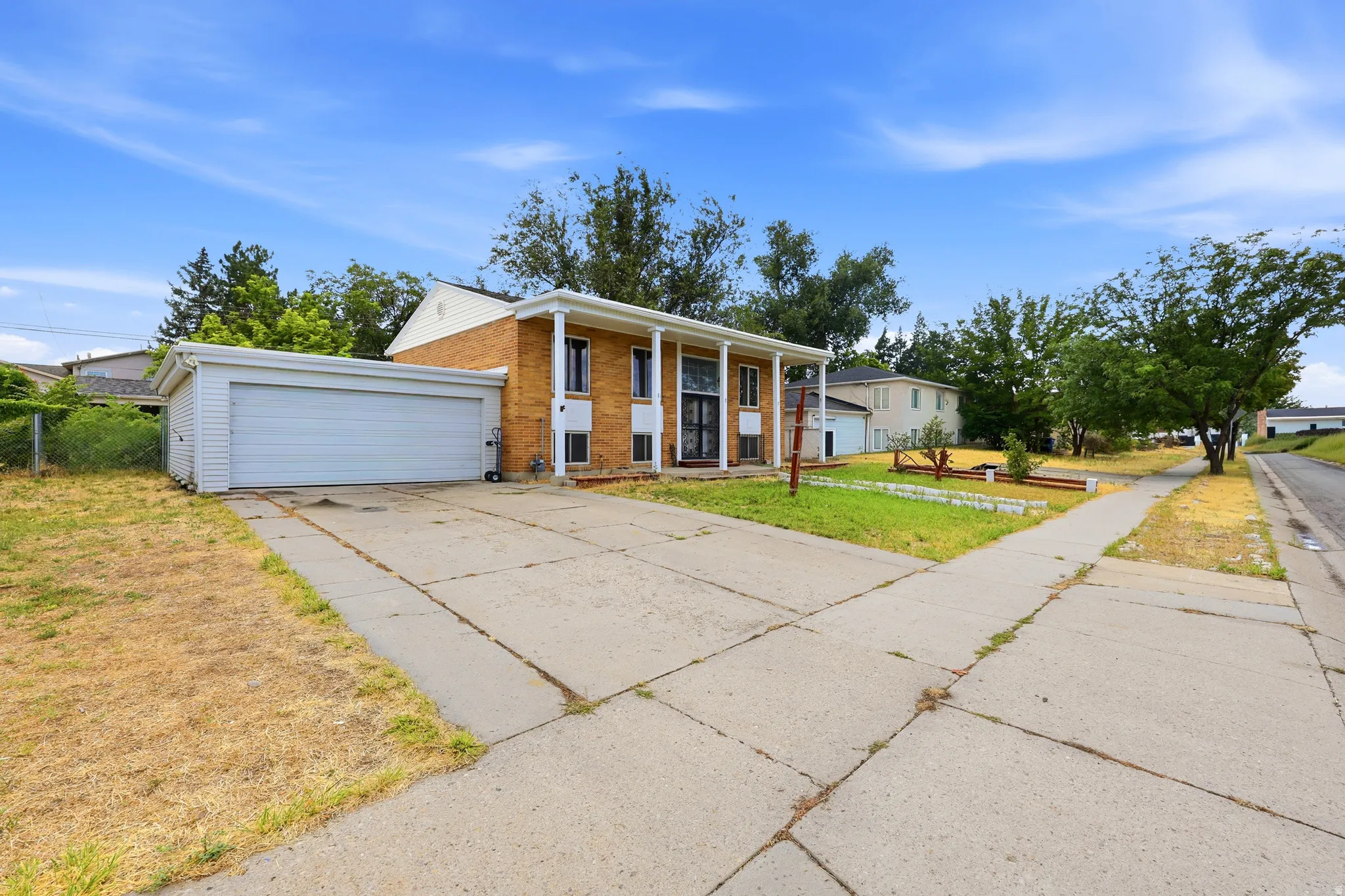 Brick exterior property featuring a two-car attached garage, expansive concrete driveway, and covered front entry with columns