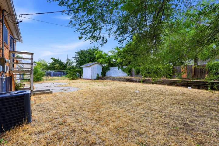 Spacious backyard featuring a storage shed, concrete patio area, and mature perimeter trees