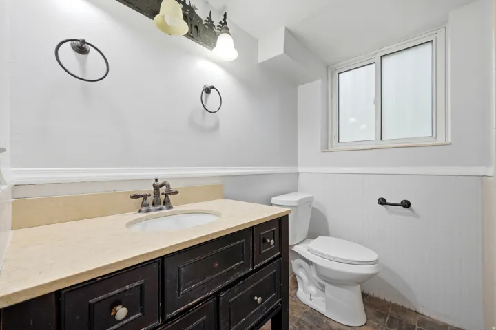 Bathroom featuring a dark wood-finish vanity with an undermount sink and light-toned countertop, a contemporary toilet, and a window providing natural illumination