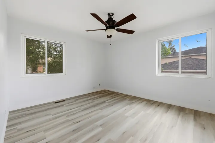 Light-filled interior featuring two windows, wood-finish flooring, a ceiling fan with integrated lighting, and neutral wall tones
