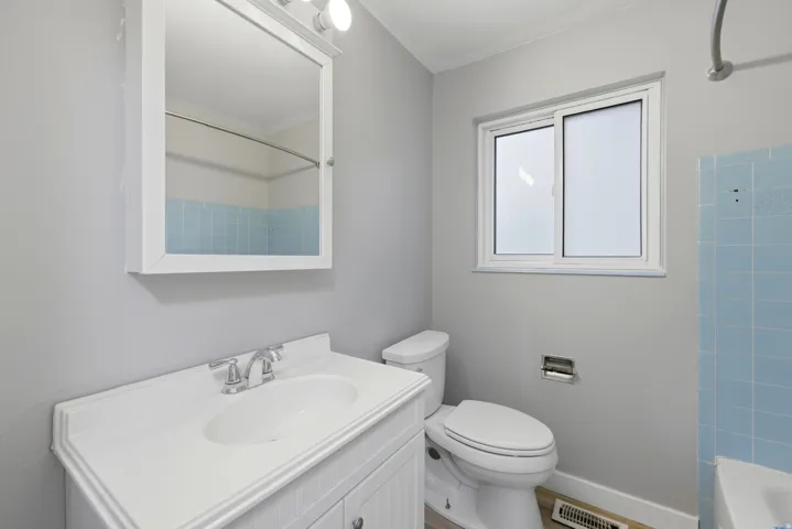 Bathroom featuring a white vanity with integrated sink, chrome faucet, wall-mounted medicine cabinet with integrated lighting, and a sliding window